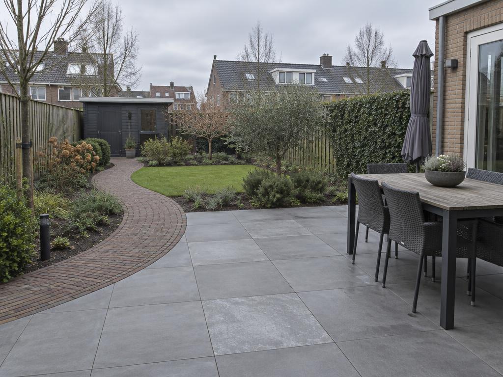 Terras van grote grijze tegels met een gebogen klinkerpad